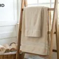 Soft beige bath towel on wooden ladder shelf, with matching rolled towels in basket, ideal for luxury bathroom decor and towel supply.